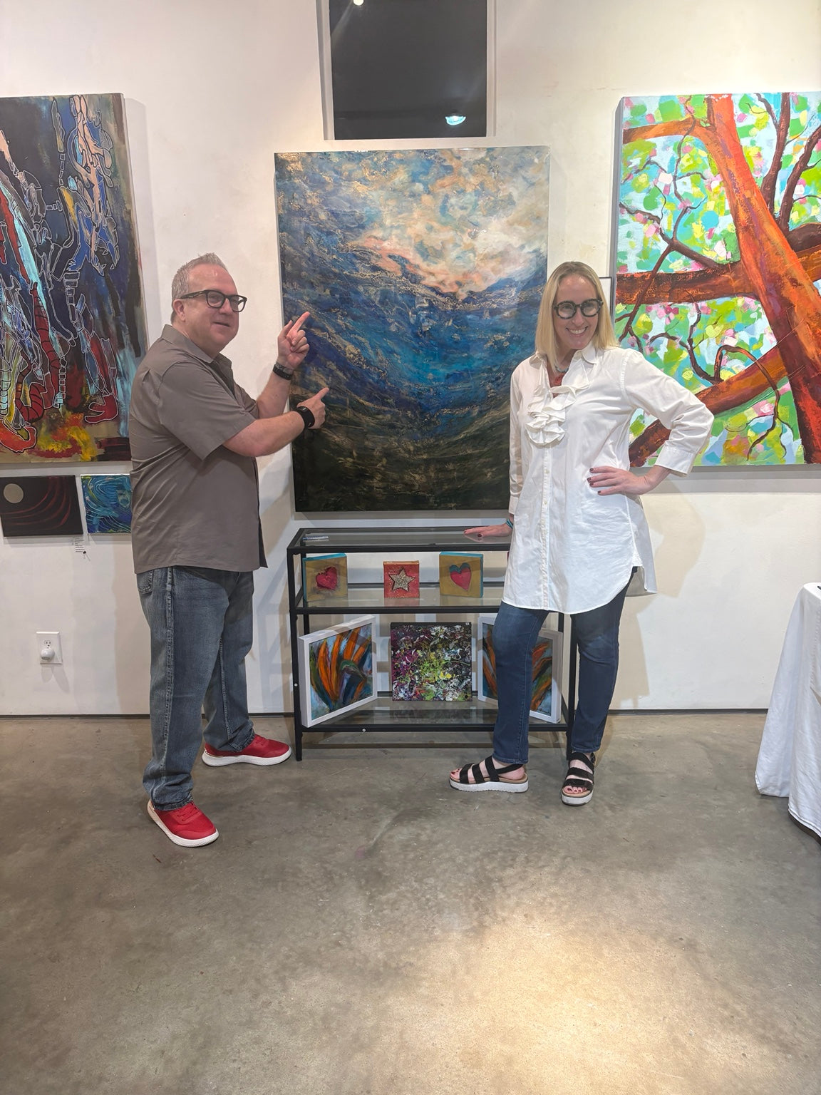 Two people beside a large blue abstract painting in a gallery.
