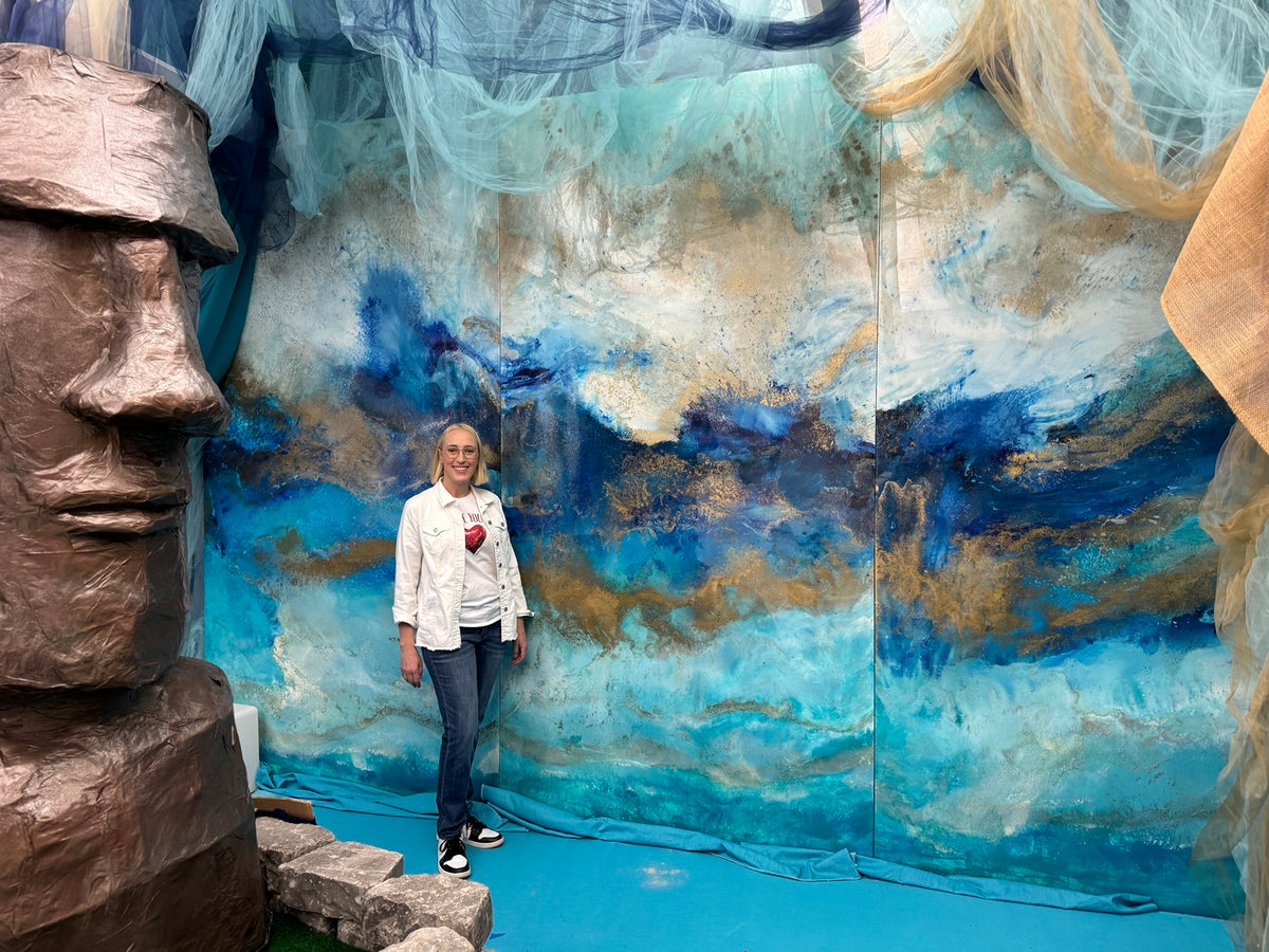 Artist beside a monumental blue, turquoise, and gold multi-panel installation.
