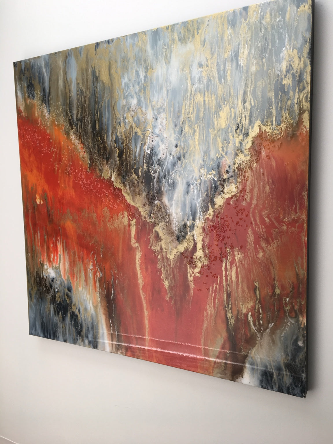 Orange, gold, gray, and white abstract painting photographed on a wall.