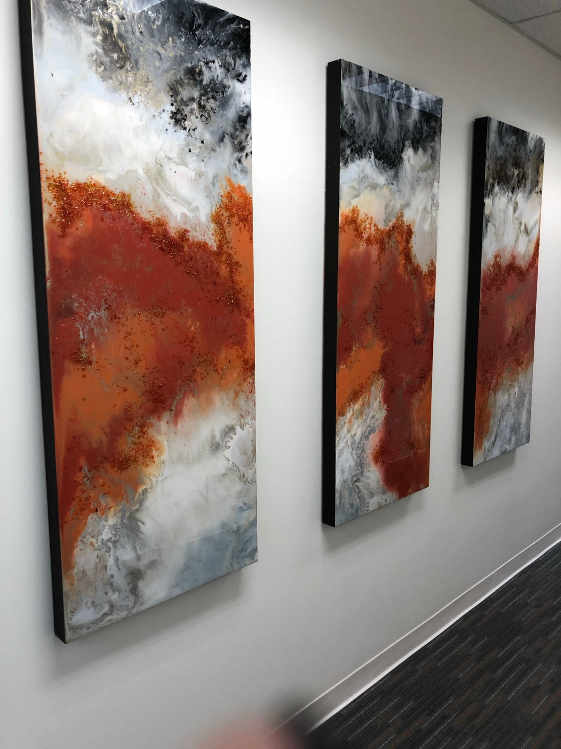Three orange, black, and white abstract panels installed along a corridor.