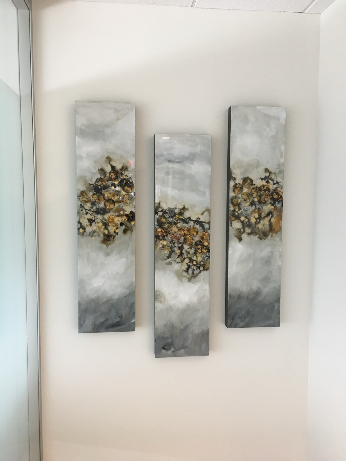 Three slender gray and gold mixed media panels in a staggered arrangement.