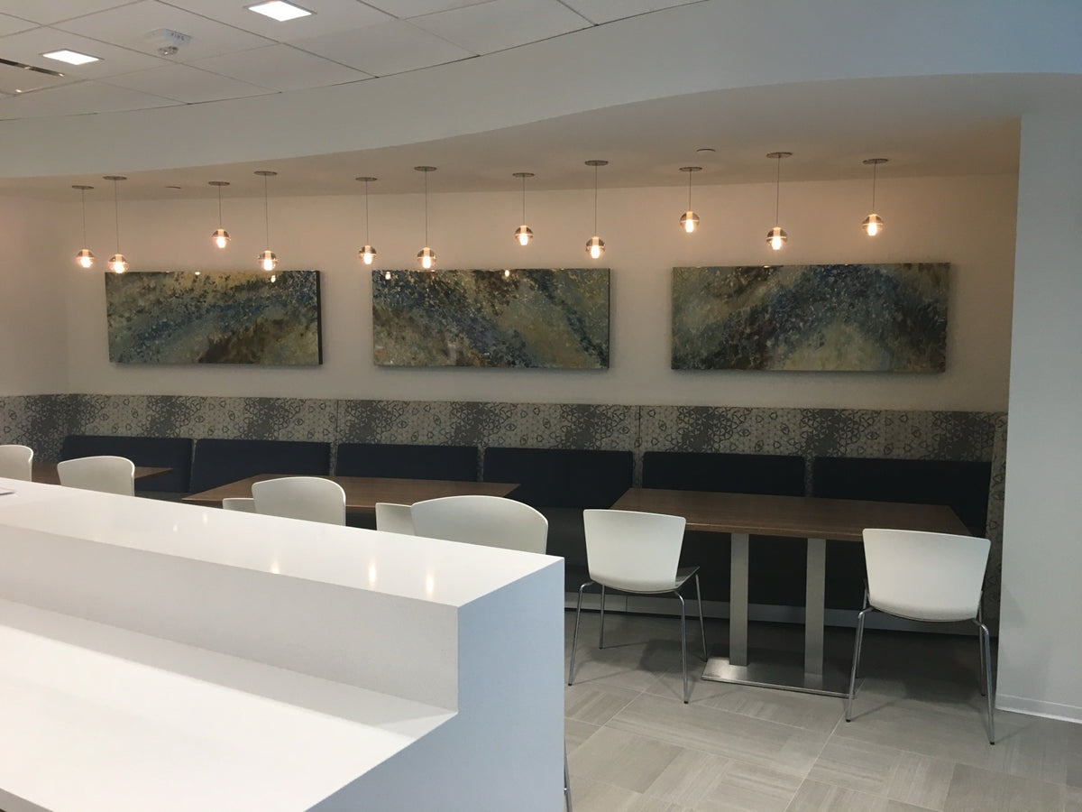 Three horizontal abstract paintings above seating in a shared interior.