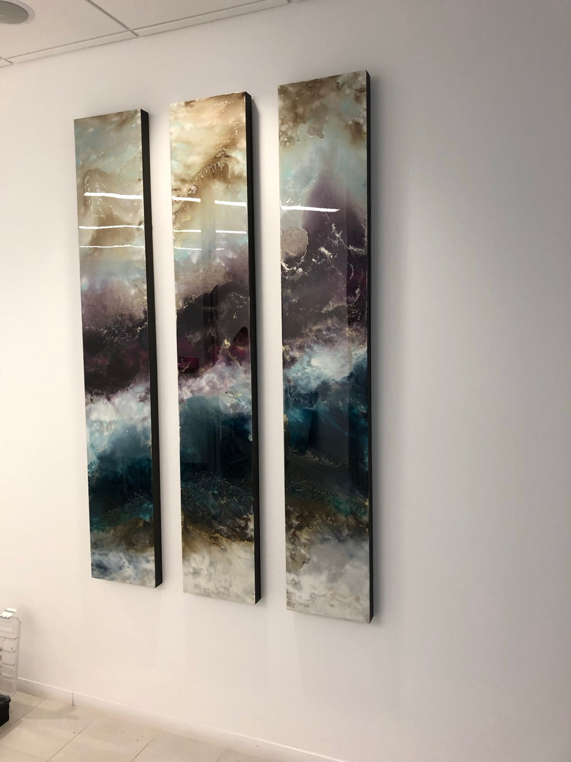 Three slender blue, plum, and gold abstract panels installed together.