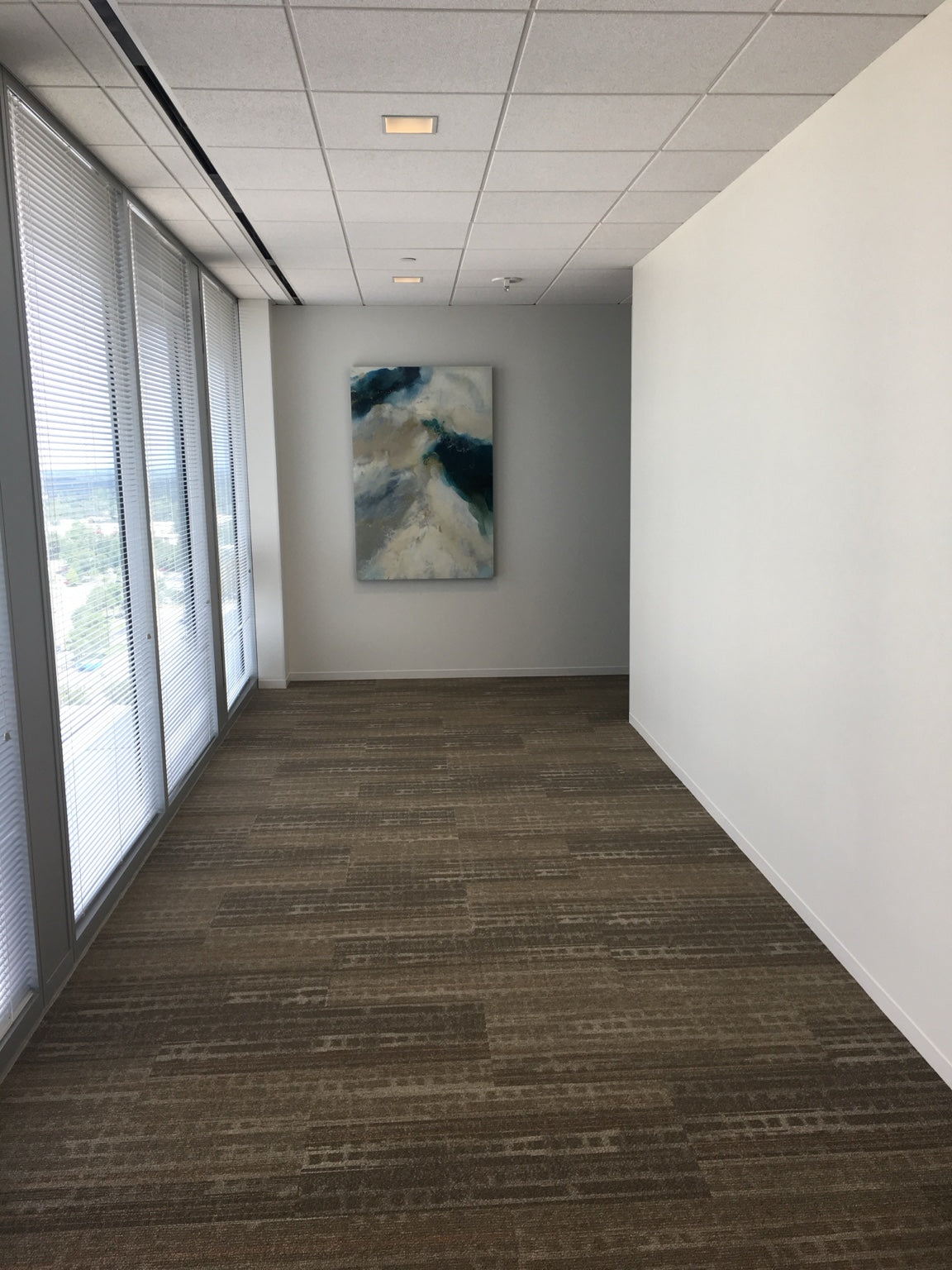 Blue and cream abstract painting at the end of a windowed corridor.